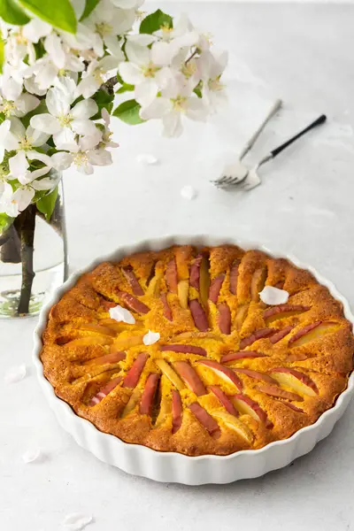 Yuvarlak bir fırında lezzetli elmalı turta, çiçek açan elma ağacı dalları.