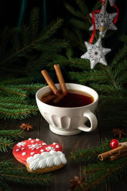 Siyah çay ve tarçınlı seramik kupa koyu ahşap bir zemin üzerinde köknar dalları arasında, kırmızı eldivenli lezzetli kurabiyeler kar taneleri, mutlu Noeller ve mutlu yıllar