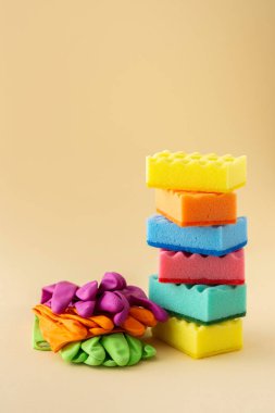 Tarafsız bej arka plan, mutfak ve temizlik konsepti üzerine bir yığın renkli bulaşık süngeri ve lastik eldiven.