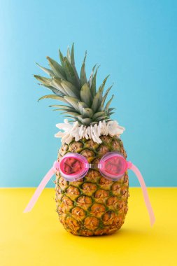 Sarı-mavi arka planda deniz kabukları olan pembe yüzme gözlüklü ananas, yaz konsepti.