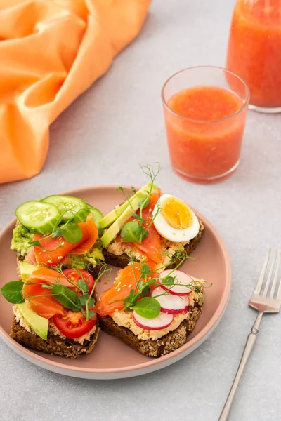 Sağlıklı lezzetli kahvaltı, avokado ve somonlu sandviçler, salatalıklar ve domatesler, turplar ve kaynamış yumurtalı bezelye, bir bardak greyfurt suyu.