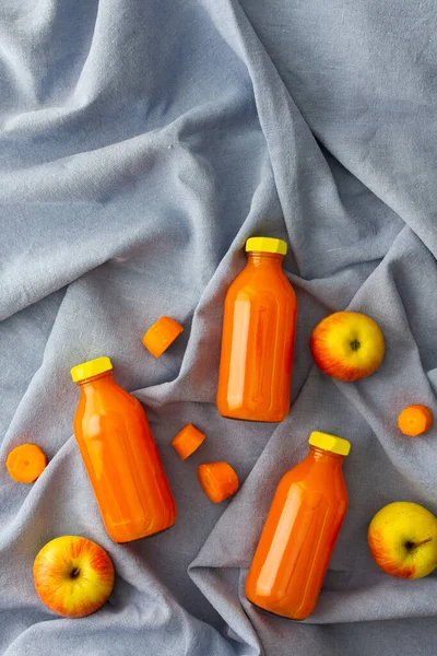 Carrot apple juice in bottles with fresh apples and carrots on a blue tablecloth, top view