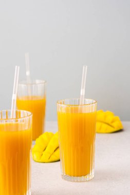 Taze sıkılmış mango suyu bardakta pipetle, olgun kesilmiş mangoyla gri arka planda.