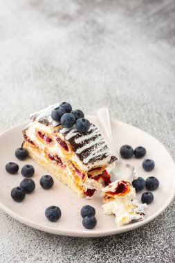 Çikolata serpiştirilmiş ısırılmış bir parça kek ve üzerine de yaban mersini serpiştirilmiş hindistan cevizi.