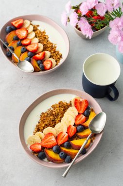 Lezzetli sağlıklı kahvaltı, yoğurtlu tahıl gevreği ve tatlı meyve, muz ve çilek, yabanmersini ve şeftali, kupada süt ve vazoda çiçekler, üst manzara