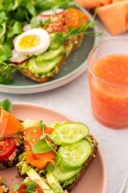 Sağlıklı lezzetli kahvaltı, avokado ve somonlu sandviç, salatalık ve domates, turp ve bezelye ile haşlanmış yumurta ve kök salatası, cam içinde greyfurt smoothie