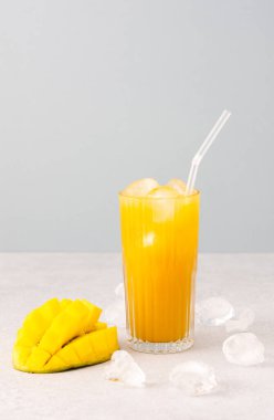Taze sıkılmış mango suyu, bardakta buzla, kamışla, olgun kesilmiş gri arka planda mangoyla.