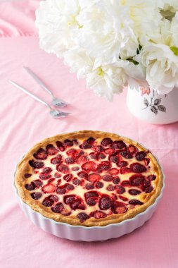 Pembe masa örtülü bir masa, bir buket şakayık ve tatlı çilekli turta, lezzetli bir yaz tatlısı.