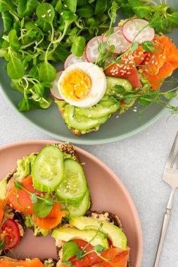 Sağlıklı lezzetli kahvaltı, avokado ve somonlu sandviç, salatalık ve domates, turp ve bezelye ile haşlanmış yumurta ve kök salatası.
