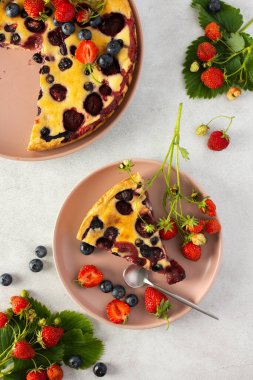 Bir parça çilekli turta. Üzerinde pembe bir tabakta taze böğürtlenler var. Gri arka planda.