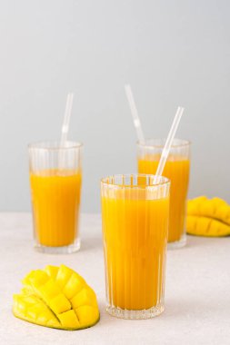 Taze sıkılmış mango suyu bardakta pipetle, olgun kesilmiş mangoyla gri arka planda.