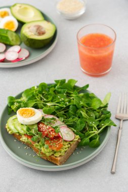 Sağlıklı lezzetli kahvaltı, avokado ve somonlu sandviç, salatalıklar ve turplar ve haşlanmış yumurta ve mısır salatalı bezelye, bardak içinde greyfurt smoothie.