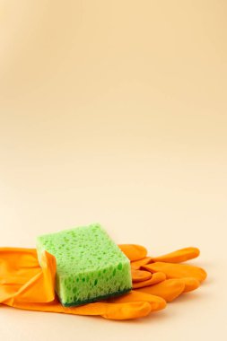 Tarafsız bej arka planda yeşil bulaşık süngeri ve turuncu lastik eldivenler, temizlik konsepti