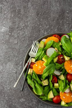 Ispanak yaprağı, mandalina ve avokado dilimleri, çekirdekli domates ve turp, çatallı bir tabakta salata, üst manzara, kopyalama alanı.