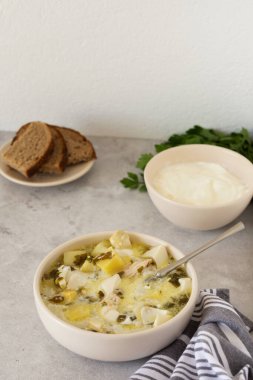 Tavuk göğsü ve kremalı patates çorbası masada bir kase çorba, ekmek ve maydanoz.