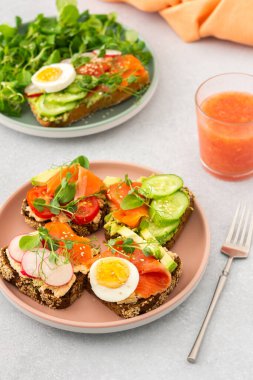 Sağlıklı lezzetli kahvaltı, avokado ve somonlu sandviç, salatalık ve domates, turp ve bezelye ile haşlanmış yumurta ve kök salatası, cam içinde greyfurt smoothie