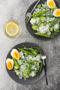 Roka salatası, salatalık ve yoğurtlu taze bezelye ve mikroyeşillikli haşlanmış yumurta, bardakta limon suyu, üst manzara.