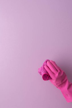 Pembe koruyucu kauçuk eldivenli bir el mor arka planda yıkanmak için mikrofiber bir bez tutar.