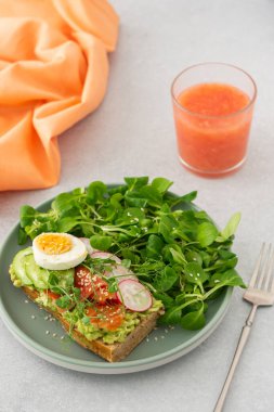 Sağlıklı lezzetli kahvaltı, avokado ve somonlu sandviç, salatalıklar ve turplar ve haşlanmış yumurta ve mısır salatalı bezelye, bardak içinde greyfurt smoothie.