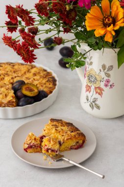 Badem taneli ev yapımı erik keki, vazoda sonbahar çiçekleri, tabakta bir dilim kek.