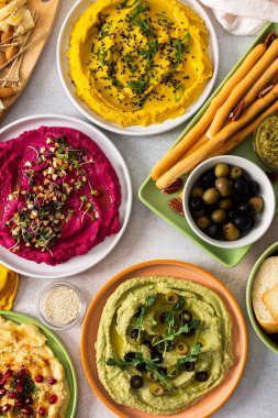 Renkli yayılmış pancar, klasik, brokoli ve zerdeçal humus, canlı malzemeler, ekmek çubukları ve çeşitli zeytinlerle bir şarküteri tahtasında sergileniyor. Toplama için mükemmel.