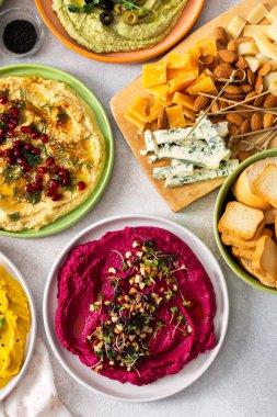Canlı bir yayışta klasik, pancar, brokoli ve zerdeçal gibi farklı türde humus sergilenir. Yanında zeytin ve ekmek çubukları ile birlikte, paylaşımı ve eğlenceyi davet eder
