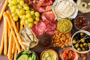 Canlı bir şarküteri kurulunda çeşitli peynirler, sosisler, humus, fındık ve sandviçler sergileniyor. Arkadaşlar güneşli bir açık hava pikniğinde toplanır, birlikte lezzetli yemeklerin tadını çıkarırlar.