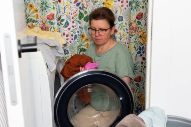 Kadınlar banyoda çamaşır makinesine çamaşır koyarken havlular ve çamaşırlarla çevrili vazifelerini dikkatle ve dikkatle yerine getiriyorlar..