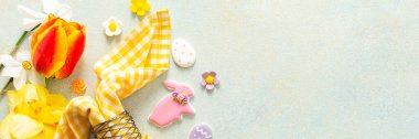 Parlak bahar çiçekleri, pastel paskalya yumurtaları, şekerler ve dekoratif elementlerle çevrili güzel bir masanın etrafını sarıyor. Tatil atmosferinin ruhunu yansıtıyor.