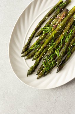 Taze otlarla kaplı buharda pişirilmiş kuşkonmaz, beyaz bir tabakta güzelce sıralanır. Yemek canlı görünüyor ve sağlıklı bir yemek ya da yan yemek için uygun.