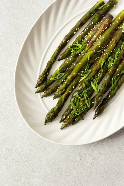 Taze otlarla kaplı buharda pişirilmiş kuşkonmaz, beyaz bir tabakta güzelce sıralanır. Yemek canlı görünüyor ve sağlıklı bir yemek ya da yan yemek için uygun.