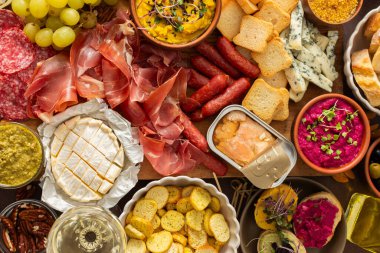 Canlı bir şarküteri kurulunda çeşitli peynirler, sosisler, humus, fındık ve sandviçler sergileniyor. Arkadaşlar güneşli bir açık hava pikniğinde toplanır, birlikte lezzetli yemeklerin tadını çıkarırlar.