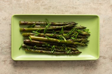 Asparagus spears are arranged neatly on a green plate, garnished with sliced green onions. This dish represents a simple yet flavorful vegetable choice for any meal