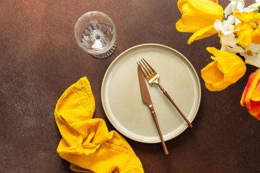 A beautifully arranged spring table setting features a light plate, gold-tone utensils, and vibrant flowers. The yellow napkin adds a pop of color, creating a joyful atmosphere for dining.