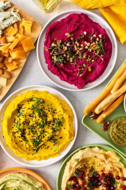 Renkli yayılmış pancar, klasik, brokoli ve zerdeçal humus, canlı malzemeler, ekmek çubukları ve çeşitli zeytinlerle bir şarküteri tahtasında sergileniyor. Toplama için mükemmel.