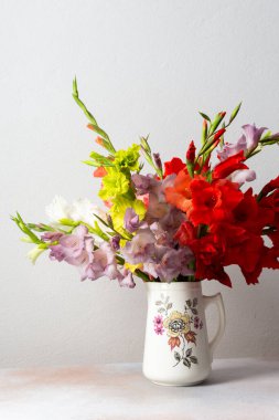 Bir vazo kırmızı ve beyaz çiçekleri de içeren çeşitli renkli gladyatörler barındırır. Düzenleme temiz bir yüzeyde duruyor, kapalı alanlara doğanın dokunuşunu ekliyor..