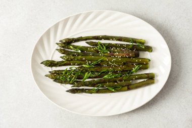 Taze otlarla kaplı buharda pişirilmiş kuşkonmaz, beyaz bir tabakta güzelce sıralanır. Yemek canlı görünüyor ve sağlıklı bir yemek ya da yan yemek için uygun.