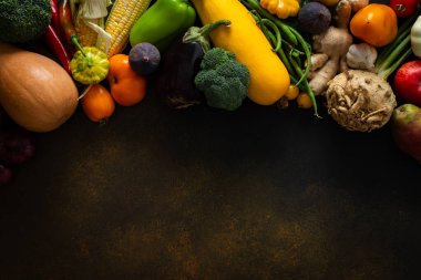 Taze sebzeler ve meyveler çeşitli renk ve şekilleri gösteren koyu bir yüzeyde düzenlenir. Bu yerel bir çiftlikten toplanan son hasattan sonra çekildi..