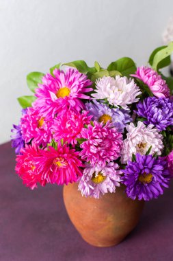 Çamur tenceresinde pembe bir masanın üzerinde düzgünce düzenlenmiş renkli çiçek karışımı bulunur. Sade bir arka planı olan ortam, doğal güzelliği ve sadeliği gösteriyor.