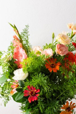 Bir buket gül, gladioli, zinya ve Eustomas suyun içinde duruyor. Yeşil uçlu havuçlar, açık arkaplana karşı düz bir masa üzerindeki düzenlemenin bir parçasıdır.