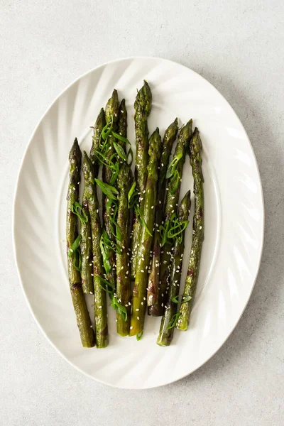 Taze otlarla kaplı buharda pişirilmiş kuşkonmaz, beyaz bir tabakta güzelce sıralanır. Yemek canlı görünüyor ve sağlıklı bir yemek ya da yan yemek için uygun.