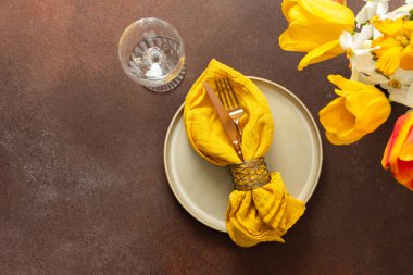A beautifully arranged spring table setting features a light plate, gold-tone utensils, and vibrant flowers. The yellow napkin adds a pop of color, creating a joyful atmosphere for dining
