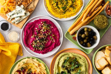 Renkli yayılmış pancar, klasik, brokoli ve zerdeçal humus, canlı malzemeler, ekmek çubukları ve çeşitli zeytinlerle bir şarküteri tahtasında sergileniyor. Toplama için mükemmel..