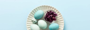 A plate holds several blue-painted Easter eggs and a couple of small patterned eggs, creating a festive atmosphere for the holiday celebration, small bowl of red cabbage, how to dye eggs blue, banner