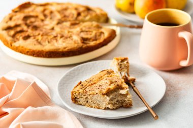Bir dilim armut turtası çatalla beyaz bir tabakta oturur. Yanında sıcak bir kahve fincanı var. Taze armutlar masaya konur, sahneye eklenir.