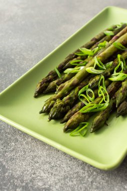 Taze ızgara kuşkonmaz üzerine doğranmış yeşil soğan modern bir mutfakta yeşil bir tabakta duruyor. Bu canlı şey sağlıklı yemek ve taze malzemeler sergiliyor.