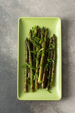 Asparagus spears are arranged neatly on a green plate, garnished with sliced green onions. This dish represents a simple yet flavorful vegetable choice for any meal