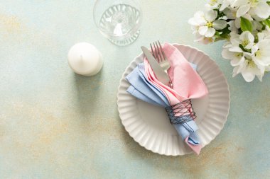A beautiful spring table setting showcases soft pastel napkins neatly arranged on a plate alongside a candle and fresh flowers, creating an inviting dining atmosphere.