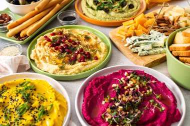 Canlı bir yayışta klasik, pancar, brokoli ve zerdeçal gibi farklı türde humus sergilenir. Yanında zeytin ve ekmek çubukları ile birlikte, paylaşımı ve eğlenceyi davet eder