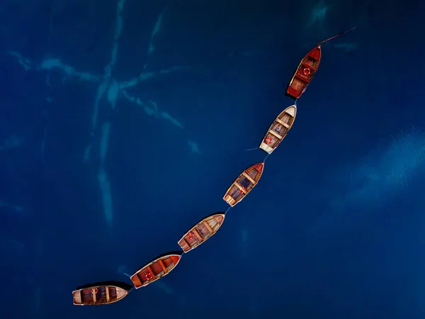 Çarpıcı bir hava fotoğrafı, sakin, derin mavi sularda ustalıkla yerleştirilmiş renkli tekneleri yakalar.